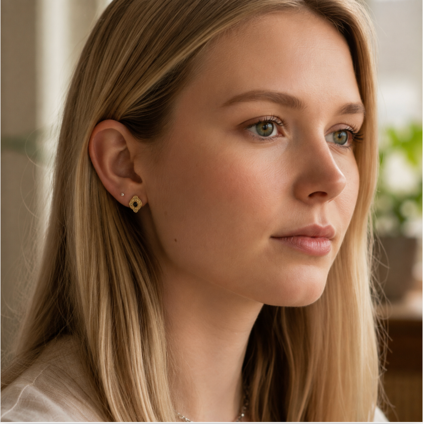 A close-up portrait of a woman with blonde hair wearing a small gold diamond-shaped earring with black stone in the center, designed by sowell jewelry.