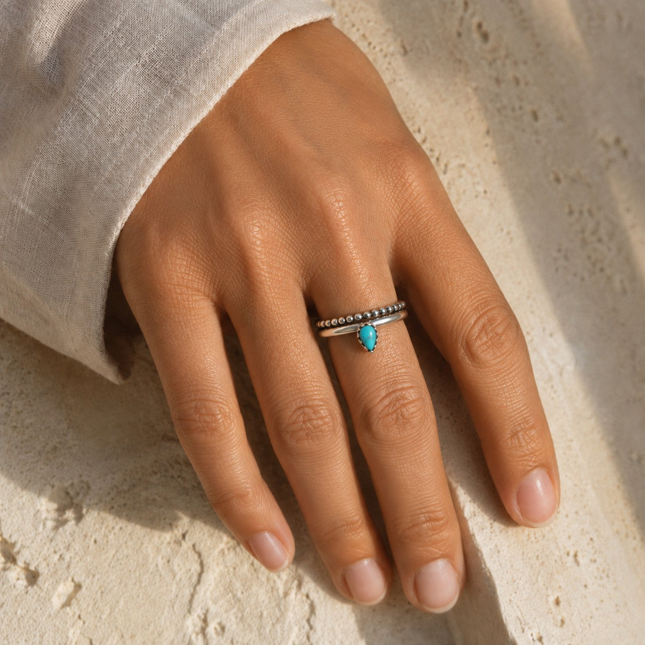 SOWELL JEWELRY Bipana turquoise ring with a sterling silver band worn on a finger against a textured stone surface.