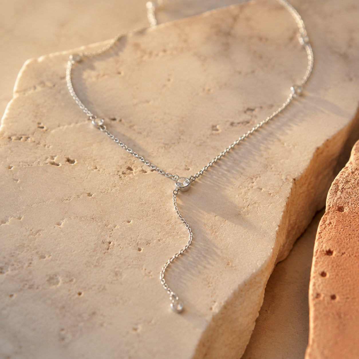 SOWELL JEWELRY Giulia lariat necklace in sterling silver with cubic zirconia bezels resting on a textured stone surface