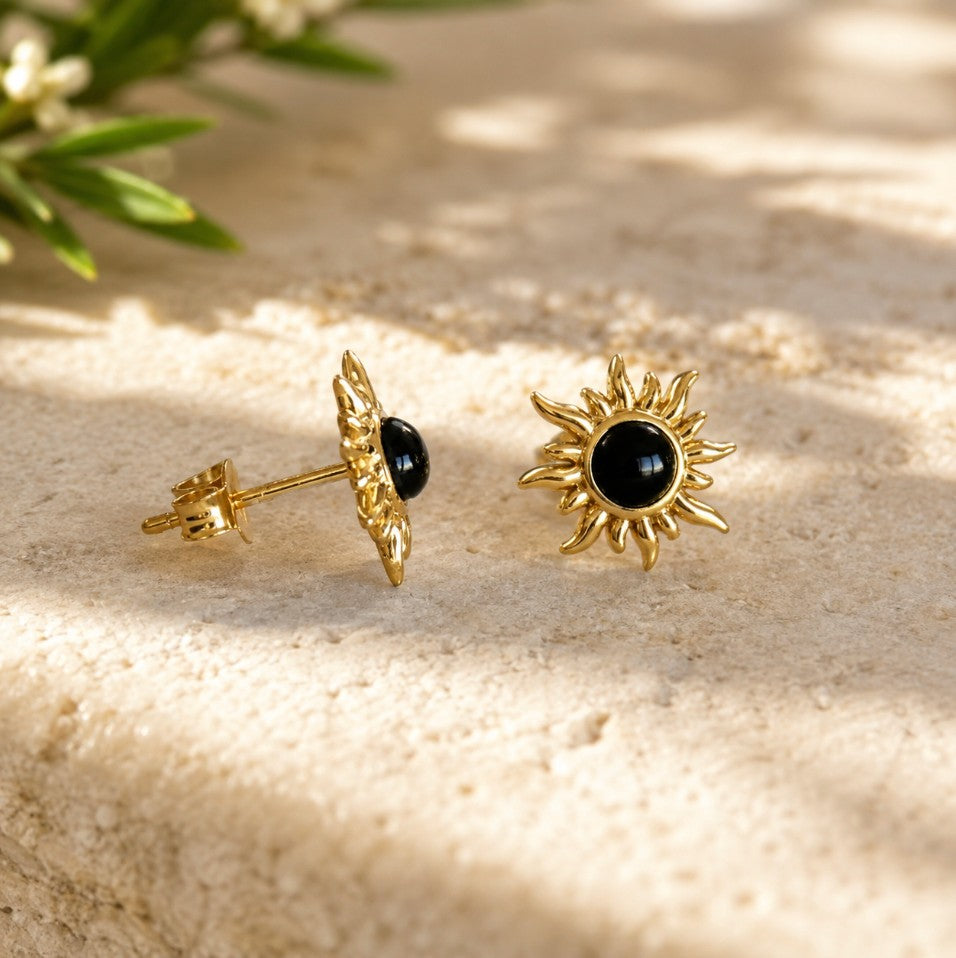 SOWELL JEWELRY 18K gold sunburst earrings featuring a central genuine black onyx stone on a textured stone surface.