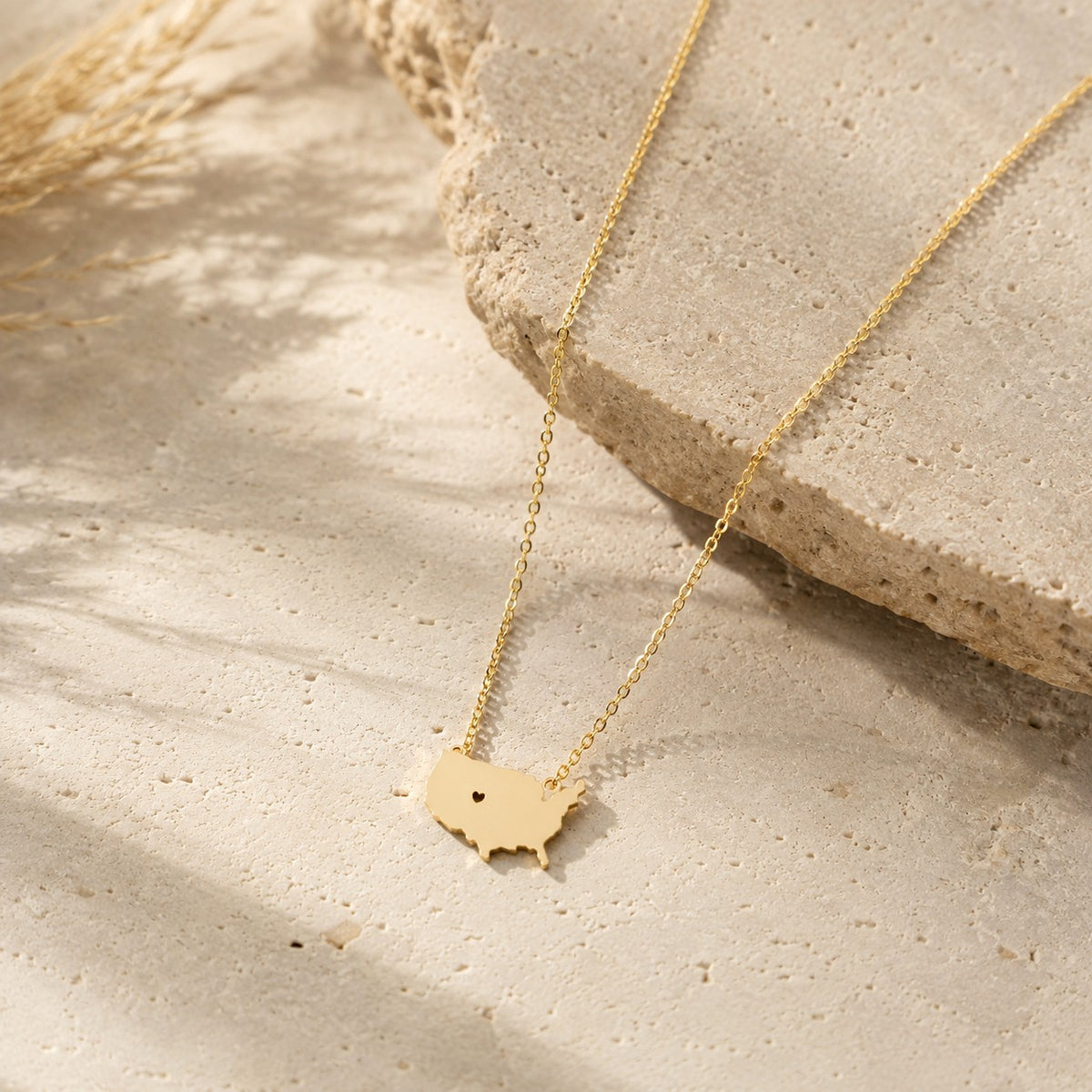 SOWELL JEWELRY 18K gold plated brass USA state map necklace with a small heart cutout on a textured stone background.