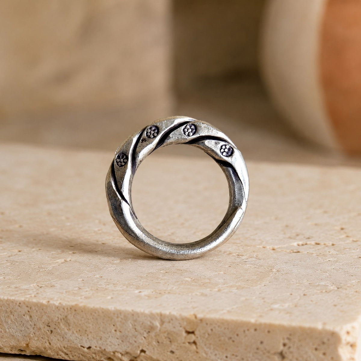 SOWELL JEWELRY Isa sterling silver band with intricate hand-carved floral details on a textured stone surface.