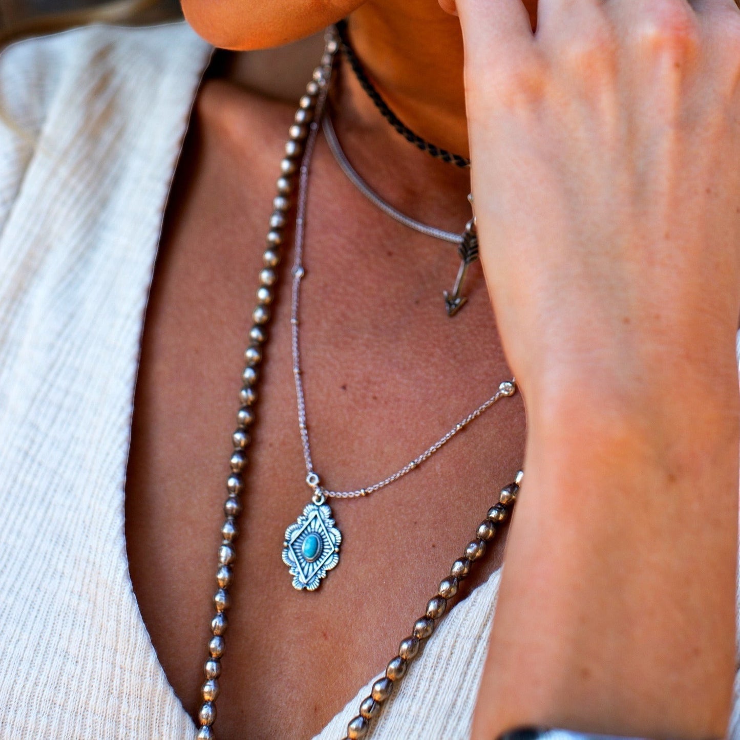 SOWELL JEWELRY Leif turquoise necklace in sterling silver worn with layered chains on a woman in a white top