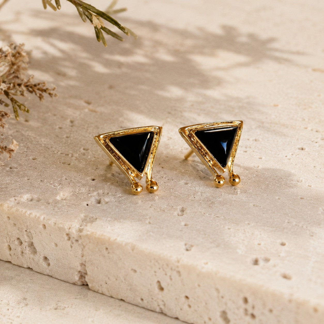 SOWELL JEWELRY Hanale triangle stud earrings featuring black onyx stones set in 18k gold vermeil on a stone surface.