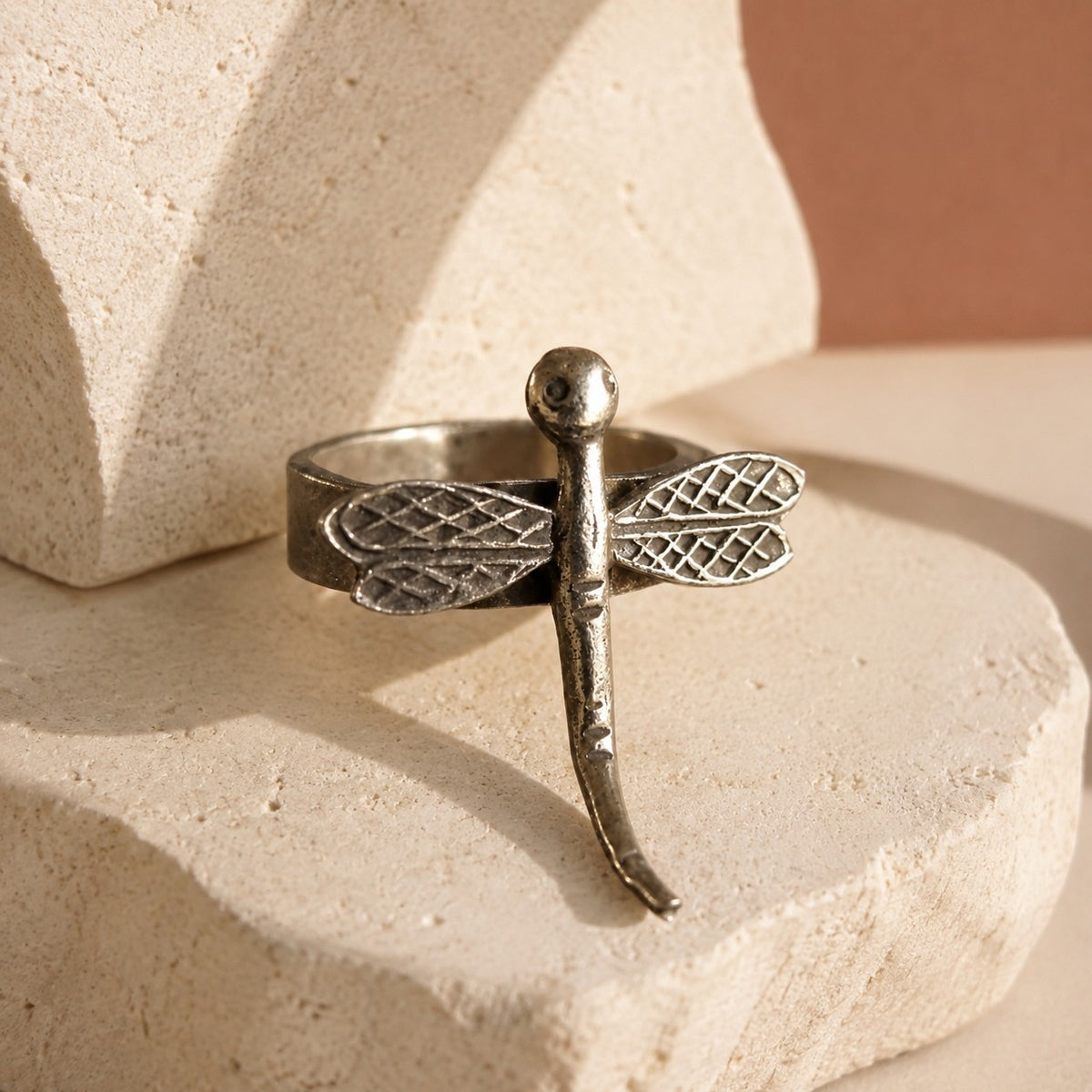 SOWELL JEWELRY handcrafted sterling silver dragonfly ring with an adjustable band on a textured stone display