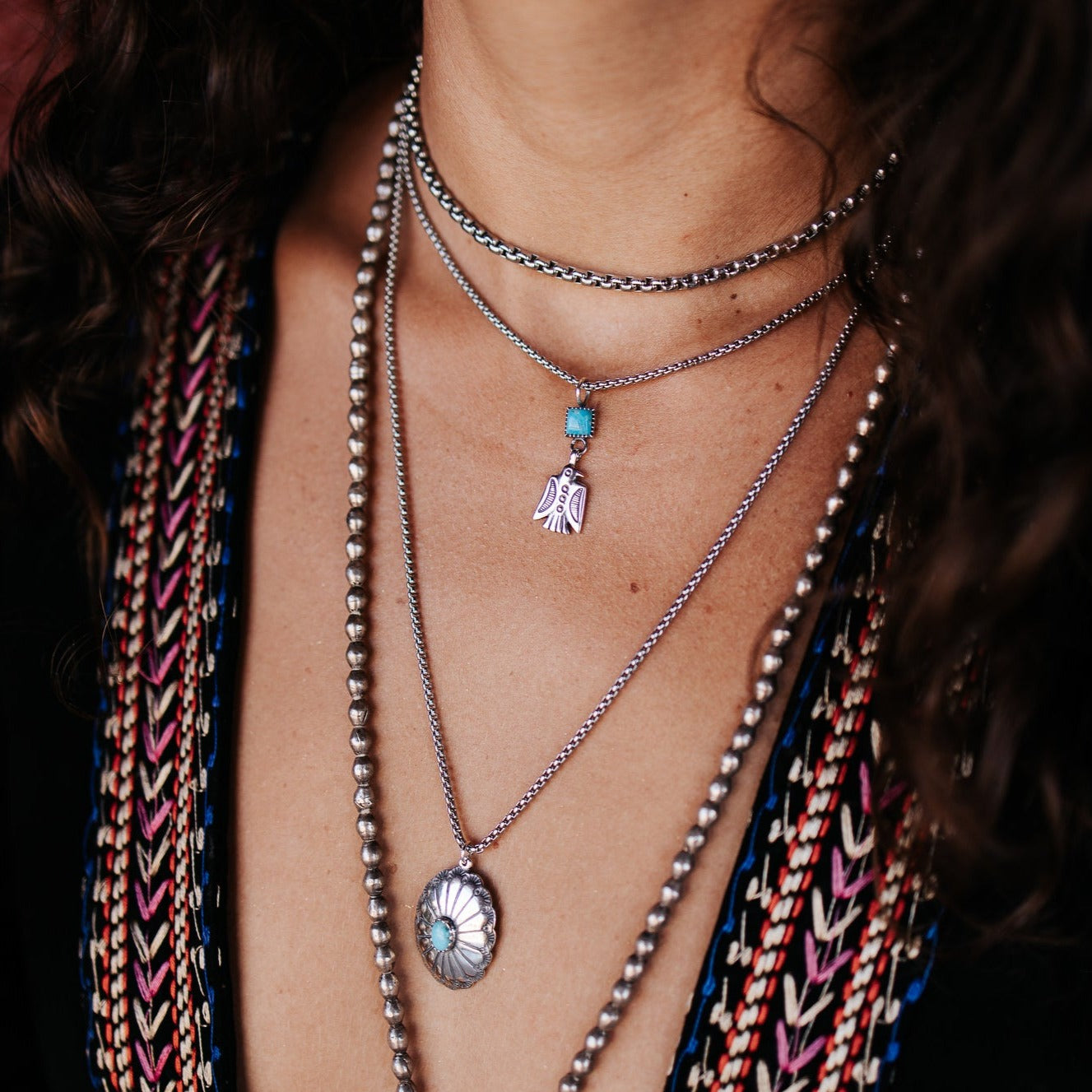 SOWELL JEWELRY Thunderbird charm necklace in sterling silver with turquoise, worn layered with other silver chains.