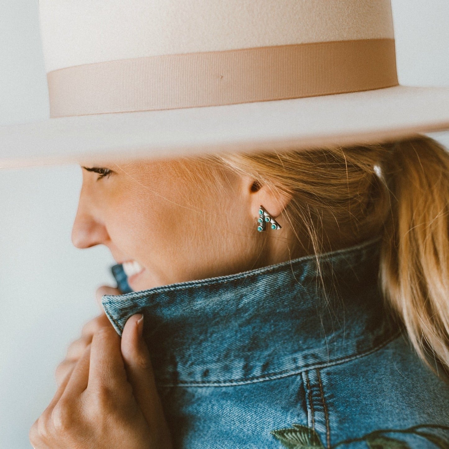 SOWELL JEWELRY Jacy crescent stud earrings with turquoise stones worn by a woman in a denim jacket and fedora