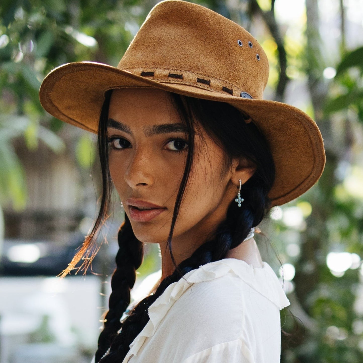 SOWELL JEWELRY turquoise cross hoop earrings in sterling silver worn by a woman in a brown suede hat