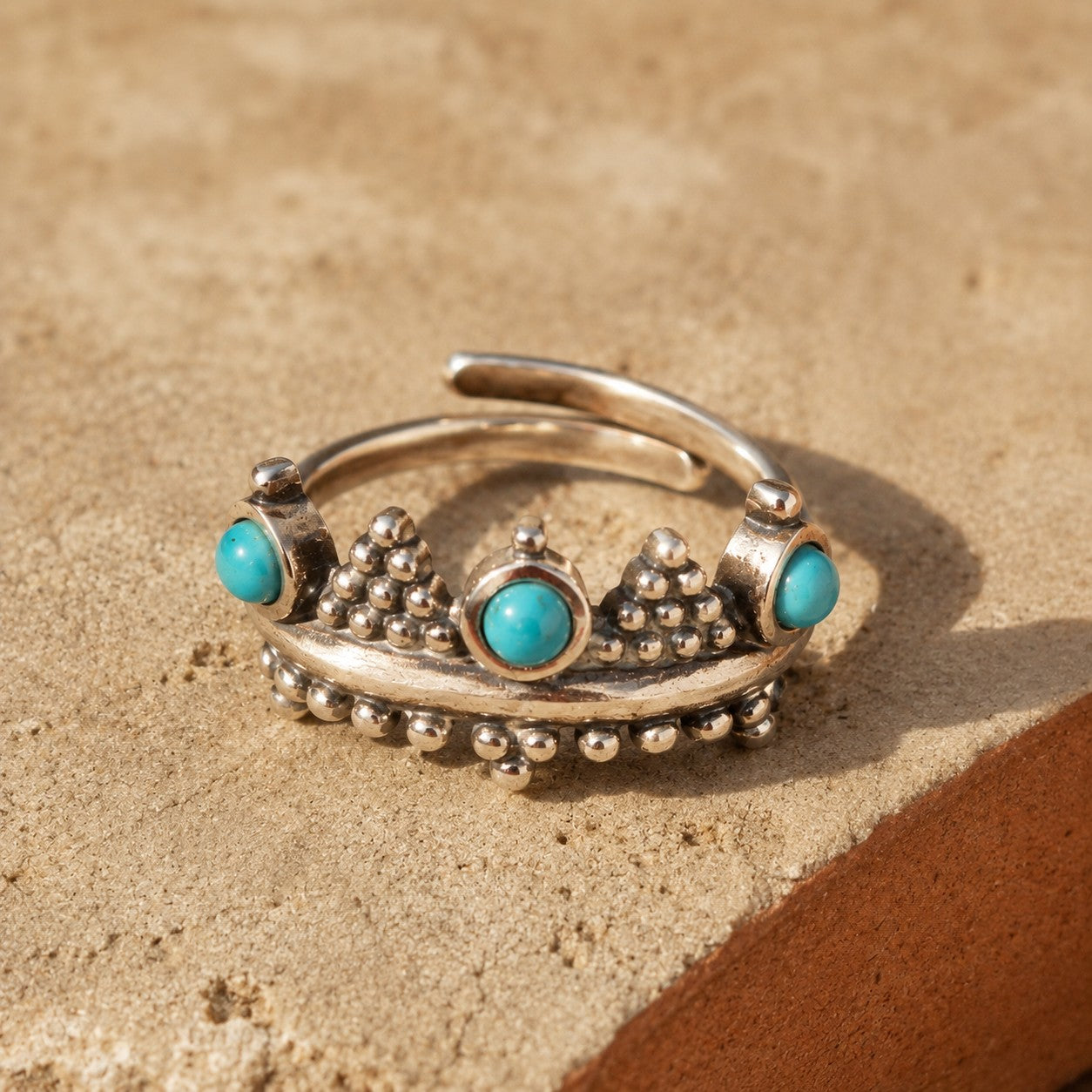 SOWELL JEWELRY sterling silver crown ring featuring three round turquoise stones on a textured stone surface