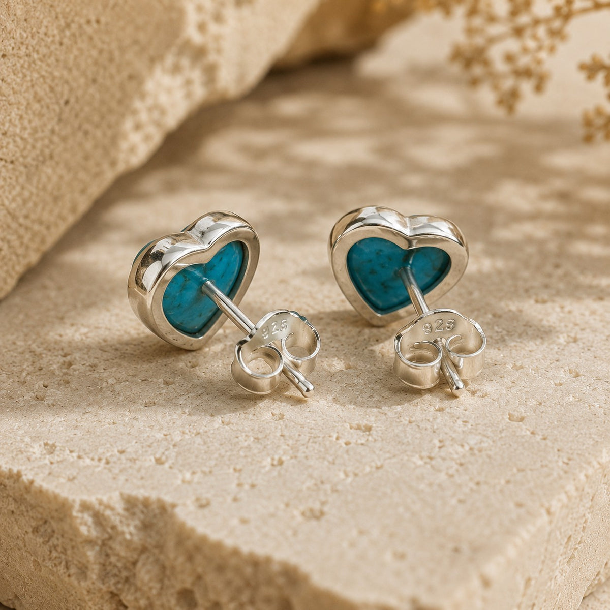 SOWELL JEWELRY turquoise heart stud earrings in .925 sterling silver resting on a textured stone surface