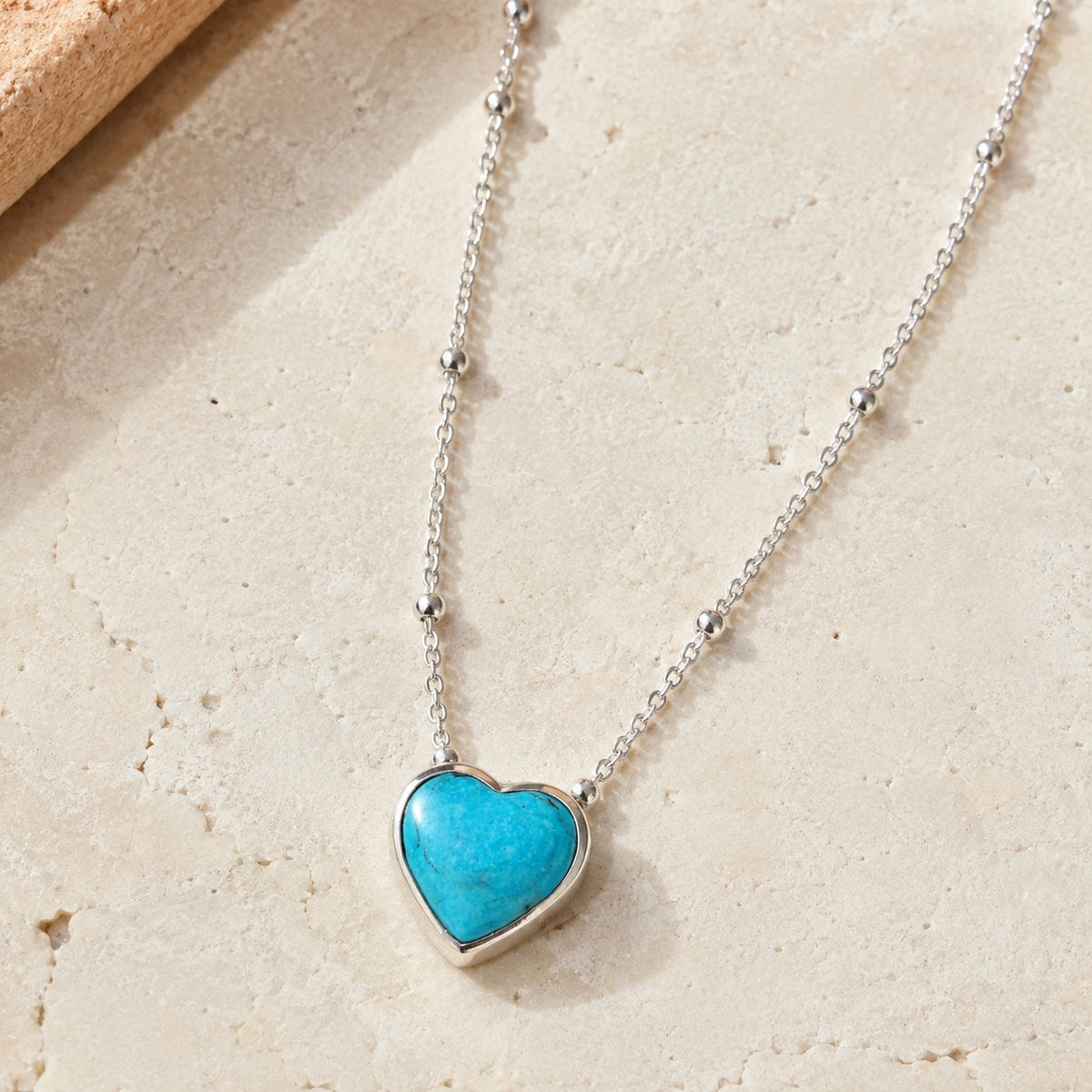 SOWELL JEWELRY heart-shaped turquoise pendant on a delicate sterling silver beaded chain against a stone background.