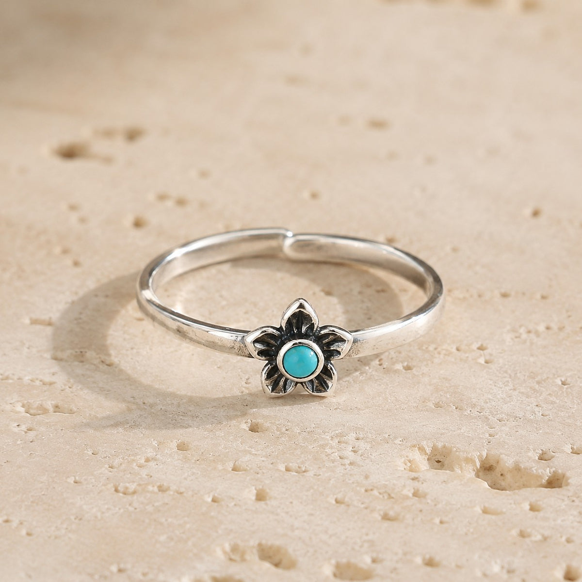 SOWELL JEWELRY sterling silver plumeria flower ring with a genuine turquoise stone on a textured stone surface