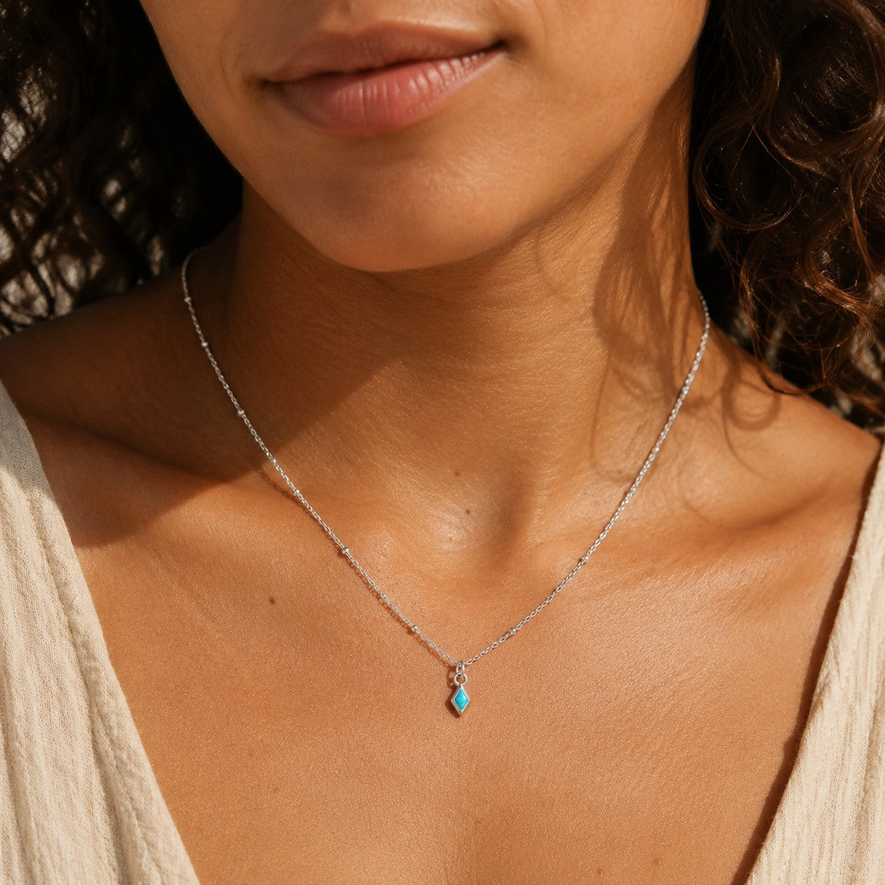 SOWELL JEWELRY delicate sterling silver necklace featuring a tiny rhombus-shaped turquoise bead worn by a woman