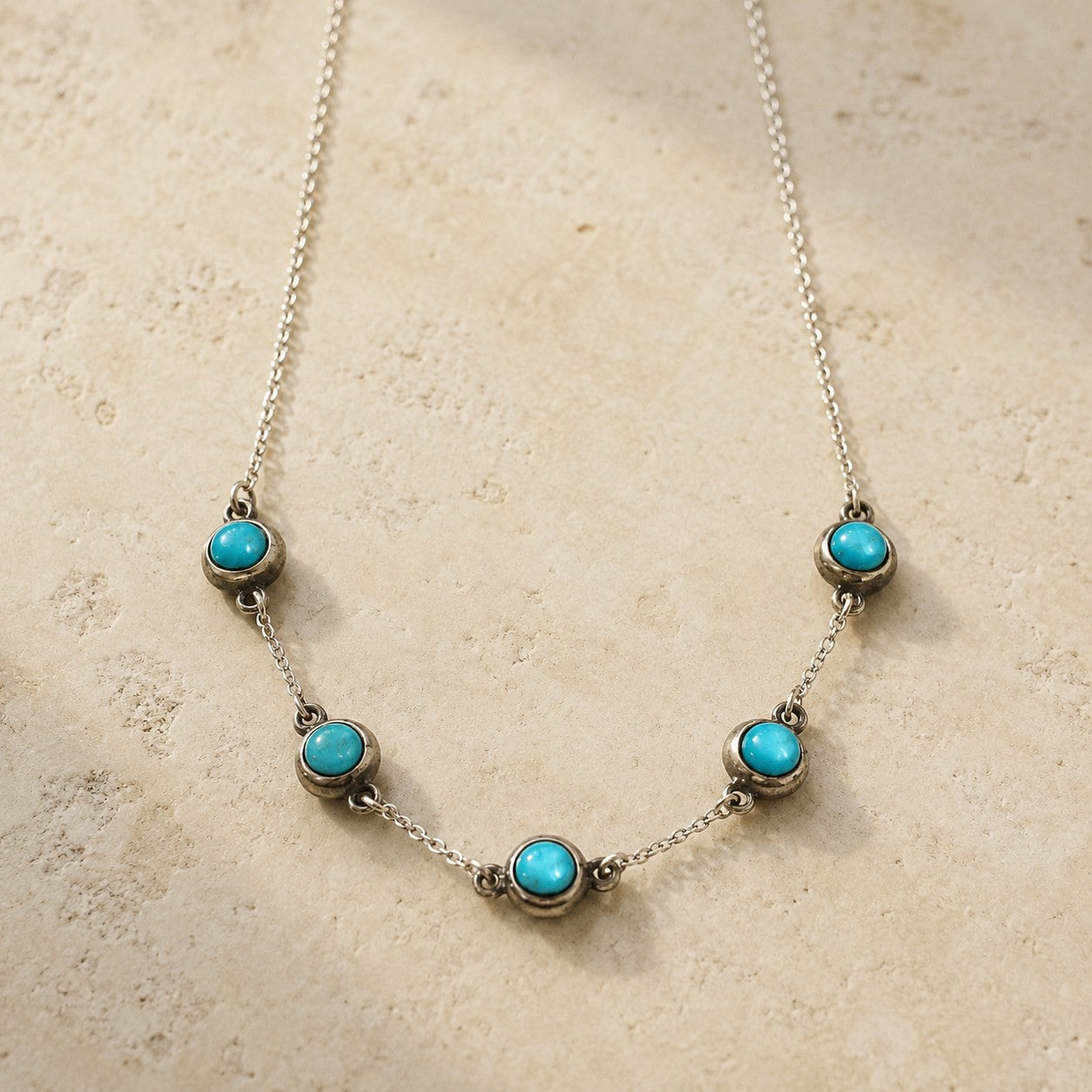 SOWELL JEWELRY 5 stone turquoise choker necklace in sterling silver with a delicate chain on a textured surface.